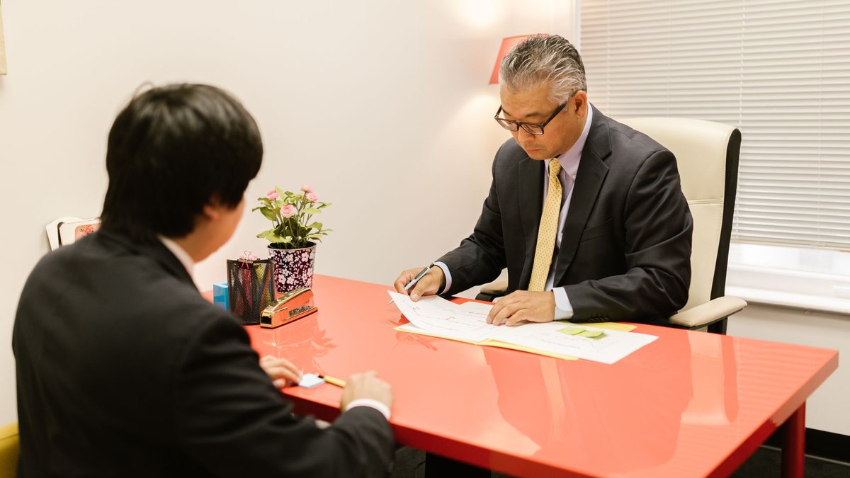 Two professionals discussing documents across a red desk in a modern office.
