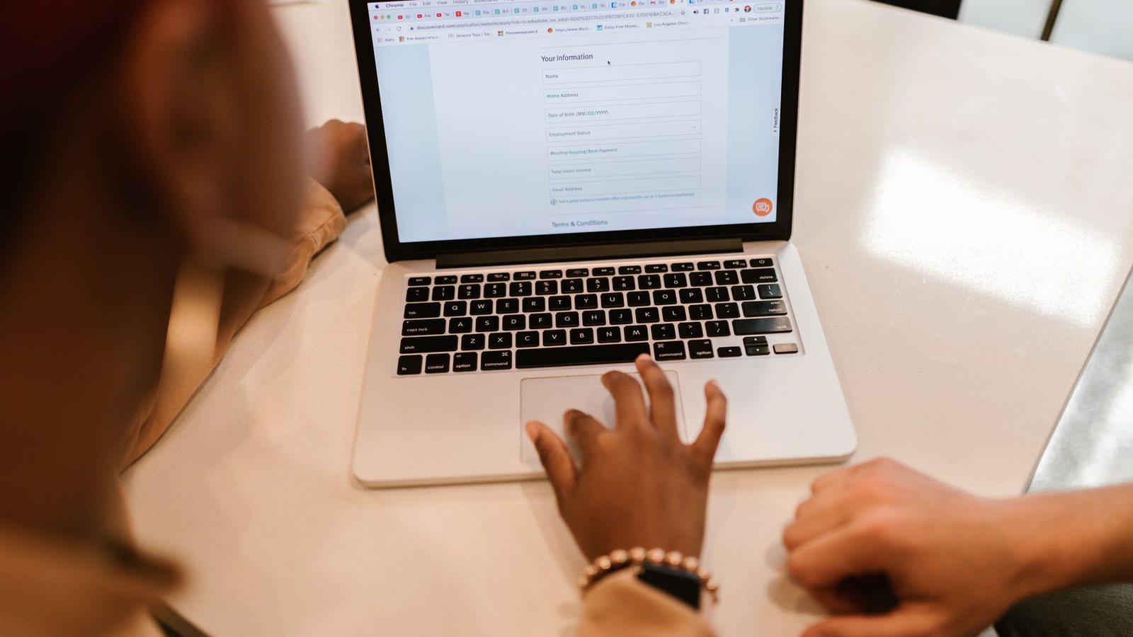 Two people working together at a laptop that is showing an online form, indoors.
