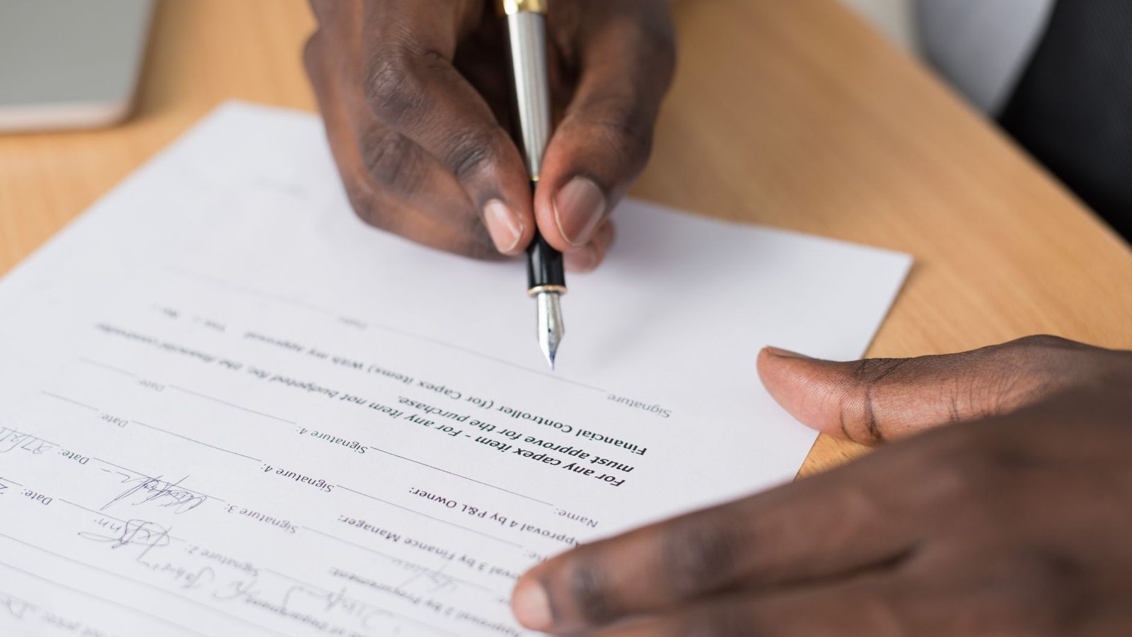 Close-up of a person's hands signing a formal document at a desk indoors.