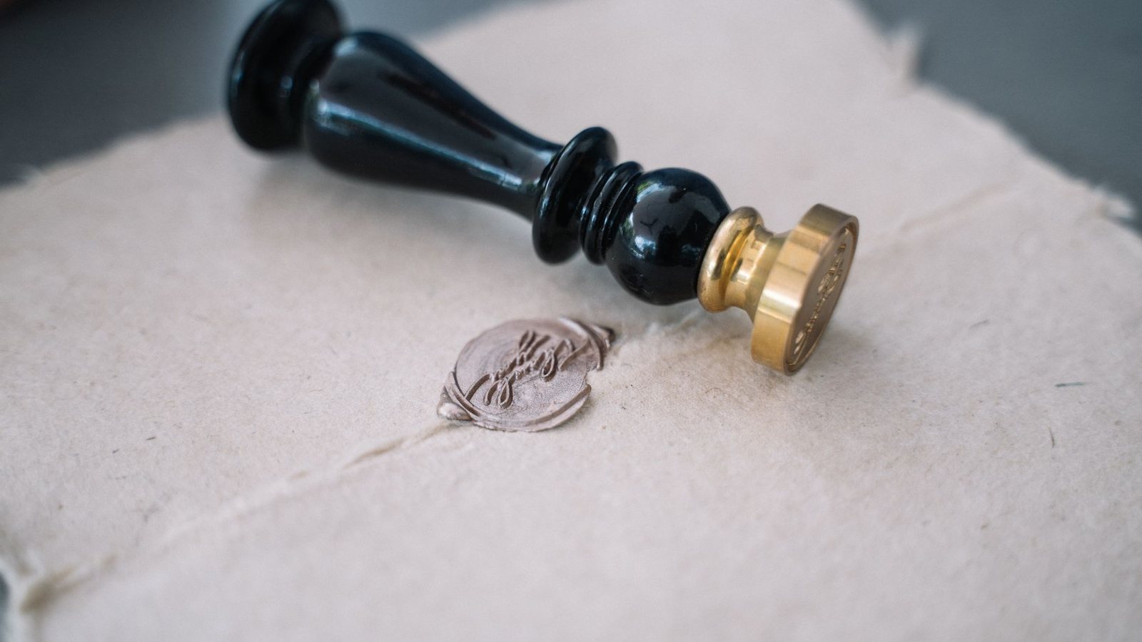A dark wax seal stamp resting beside a pressed seal on handmade paper. No text, no country markings.
